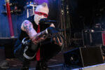 Frontman with white face paint and red eye stripe kneeling on stage and singing into a microphone.