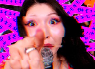Singer pointing directly at the camera while singing into a microphone, with a bright pink glitchy background behind her.