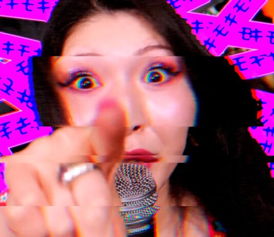 Otoboke Beaver veröffentlichen neues Album Singer pointing directly at the camera while singing into a microphone, with a bright pink glitchy background behind her.