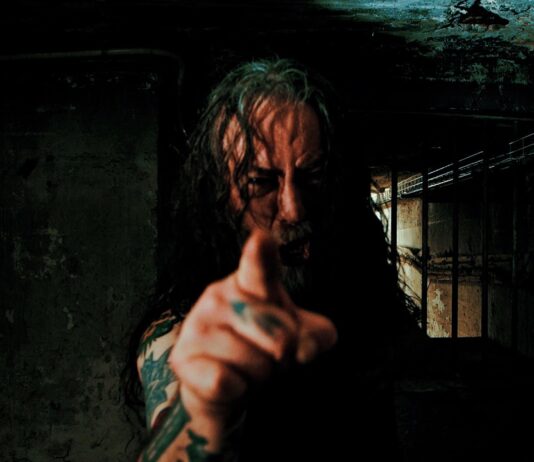 Benediction kündigt Besetzungswechsel an Man with long hair and tattoos points at the camera in a dark, grimy basement; Nuclear Blast Records logo appears in the bottom-left corner.