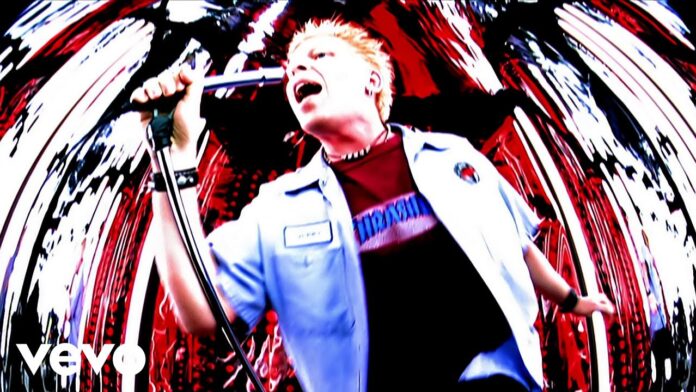 The Offspring veröffentlichen 4″-Single von „Pretty Fly“ Male singer with blonde hair performs into a microphone on a vibrant, swirling red-and-white concert backdrop (Verve logo visible).