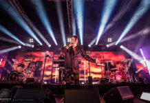 Das war das Amphi Festival 2025 Male lead singer with microphone center stage, band performing with drums and keyboard under bright concert lights.