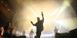 Dropkick Murphys 24.07.26, Store Vega, Kopenhagen Male lead singer on a bright concert stage, mic raised, striking a dynamic pose toward the crowd with band members and lights in the background