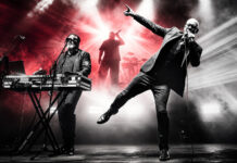 Amphi Festival 2026: Covenant springen für VNV Nation ein Band on stage: singer with microphone to the right, keyboardist on the left, drummer in back, dramatic red and white lights filling the scene.