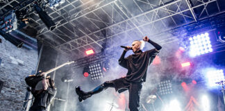 Castle Rock Festival 2026: Der letzte Vorhang auf Schloss Broich Vocalist onstage mid-leap with microphone, guitarist behind on left, dramatic stage lights and smoke surround a rock concert.