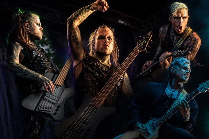 Klaas Helmecke und Pi Stoffers verlassen Lord Of The Lost Four metal musicians onstage during a high-energy performance; center bassist raises a fist while two guitarists play intensely under colorful stage lights.|center musician with long blond hair raises fist while playing bass, flanked by two guitarists, all in black stage outfits