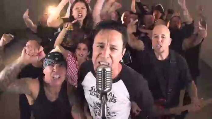 Lou Koller (Sick Of It All) ist gestorben Lead singer at a vintage microphone with an animated crowd cheering behind him in a band setting.