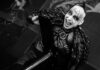 Das Ich: Bruno Kramm nach Konzert in Granada verstorben Black-and-white photo of a performer in spiked leather armor shouting while gripping a large prop weapon on stage.