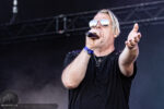 Male singer on stage wearing mirrored sunglasses, singing into a handheld microphone with an outstretched hand toward the audience.