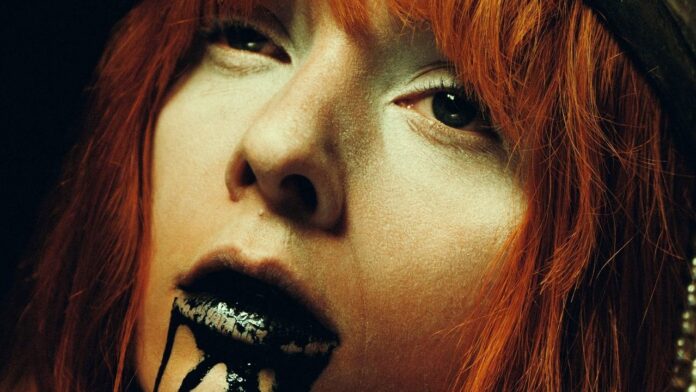 Slipknot veröffentlichen neue Single „Arsenal“ Close-up portrait of a person with orange hair and black, dripping lipstick for a dramatic makeup look.