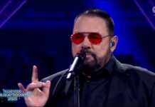 Alphaville werden aus- und wiedereingeladen beim Glücksgefühle Festival Male singer in a black suit with red sunglasses performs on stage into a microphone, blue-lit background visible.