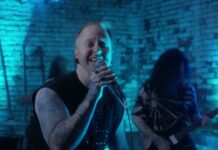 A Skylit Drive unterschreiben bei Vaux Records und veröffentlichen das Musikvideo zu „Half Hearted“ Male vocalist sings into a microphone on a blue-lit brick-walled stage; guitarist in the background with tattoos visible on his arms.