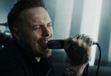 Architects veröffentlichen Video-Single „Machine“ Male vocalist with tattoos screaming into a handheld microphone, eyes closed, in a moody studio setting.