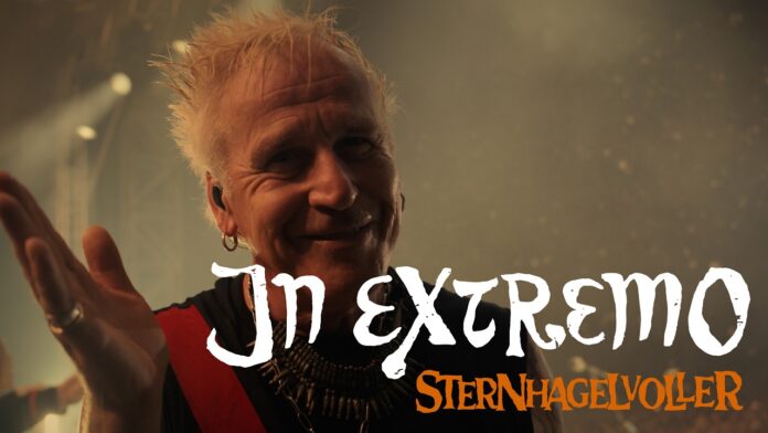 In Extremo: Neues Video „Sternhagelvoller“ vereint die Mittelalter-Rock-Szene Smiling male singer on stage with spiky blonde hair; white handwritten text 'In Extremo' and orange text 'Sternhagelvoller' overlay across the image.